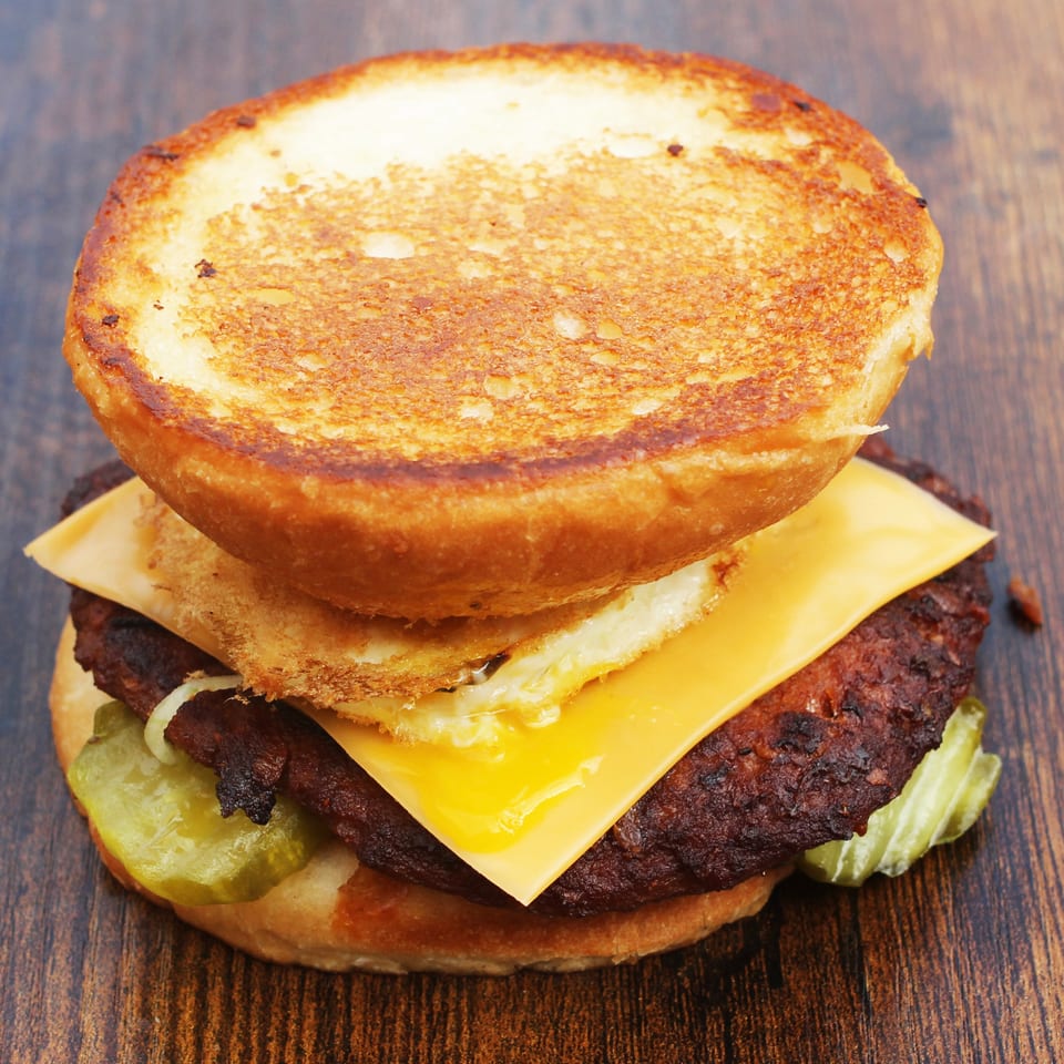 Double cheeseburger with toasted bun, two beef patties, melted cheddar cheese, and pickles on a wooden table.