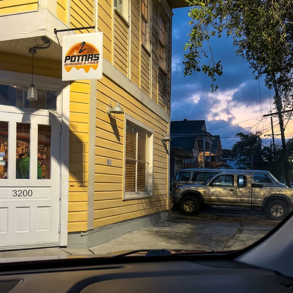 Yellow Potras Burgers & Fries storefront with white entrance door, street number 3200, parked vehicles, and evening trees.